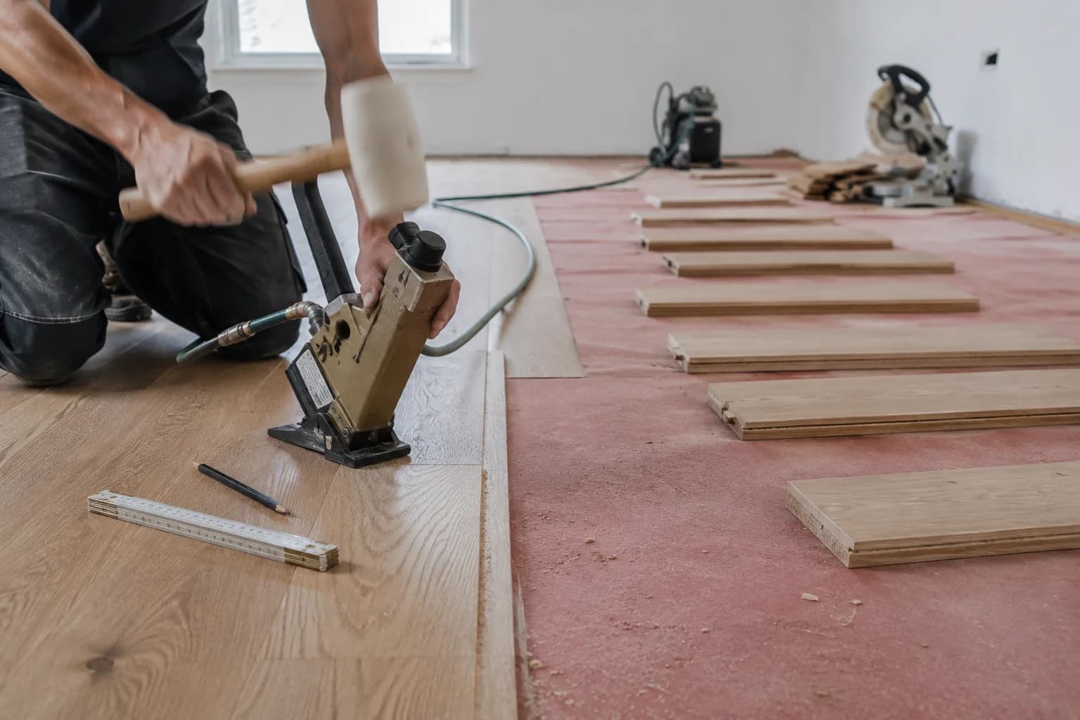 Craftsman nailing down hardwood planks over underlayment
