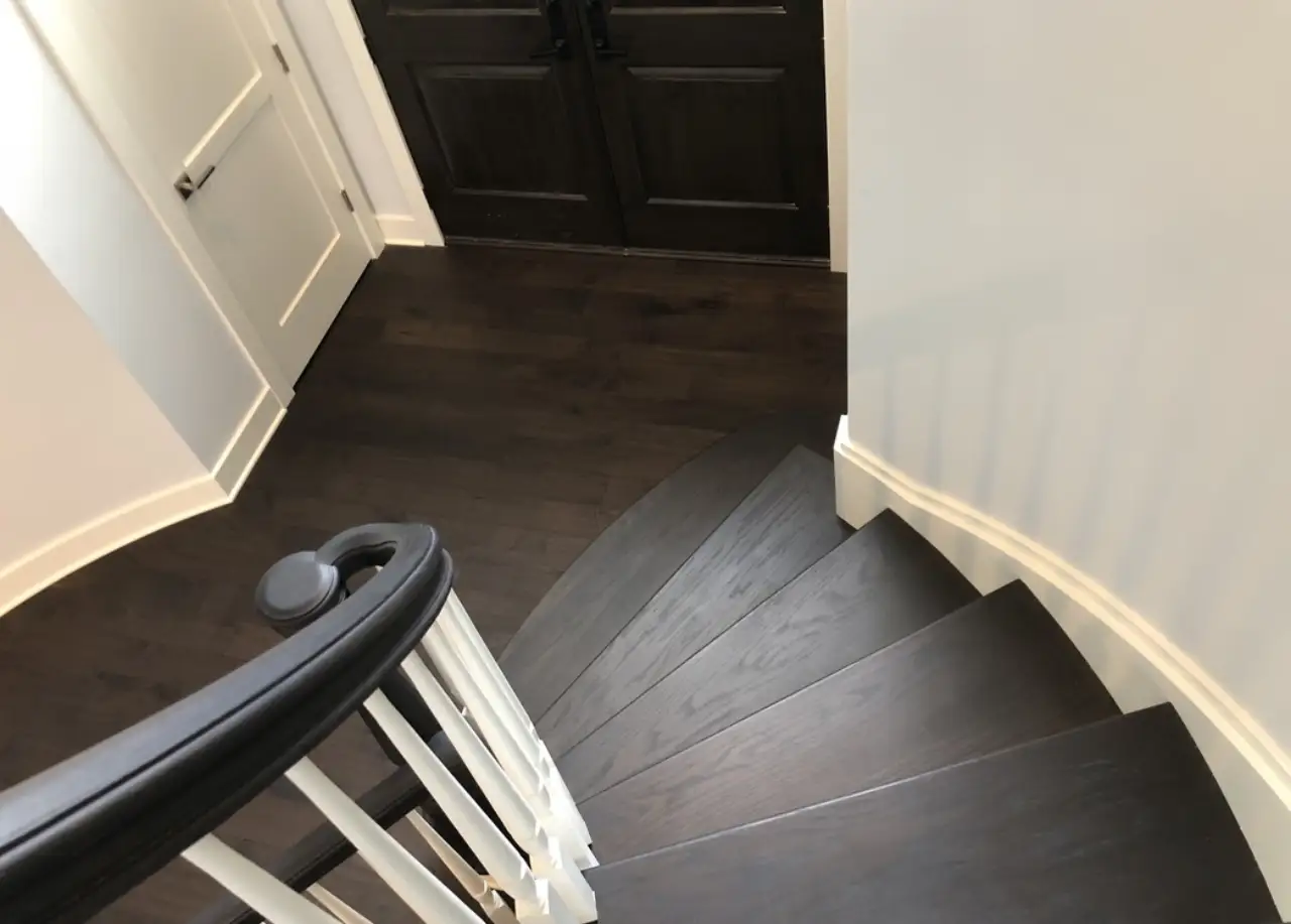 Curved dark walnut staircase winding down to a walnut entry floor — custom eight-inch FAS walnut, Northville